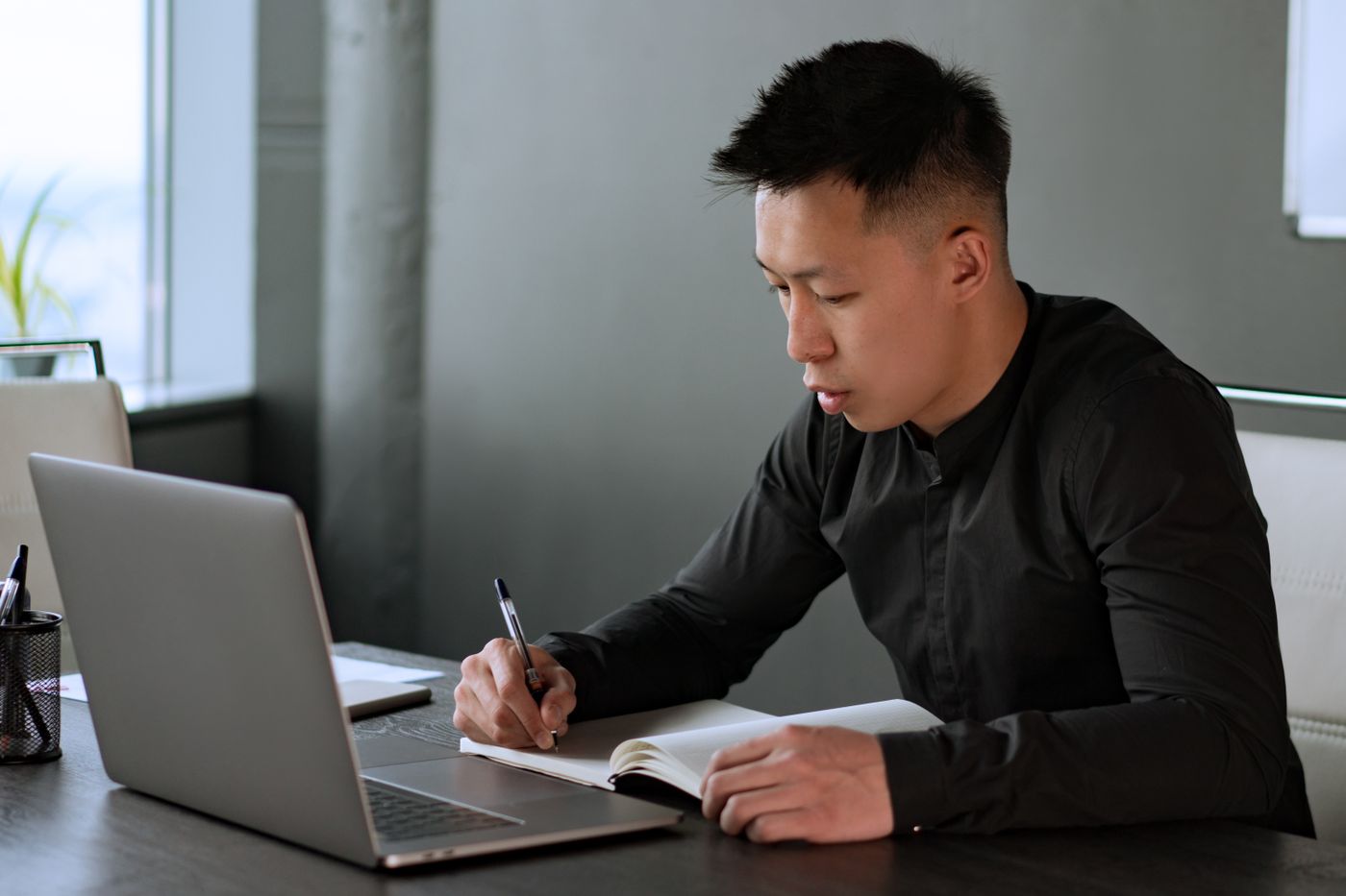 An office worker writing notes at a desk with a laptop